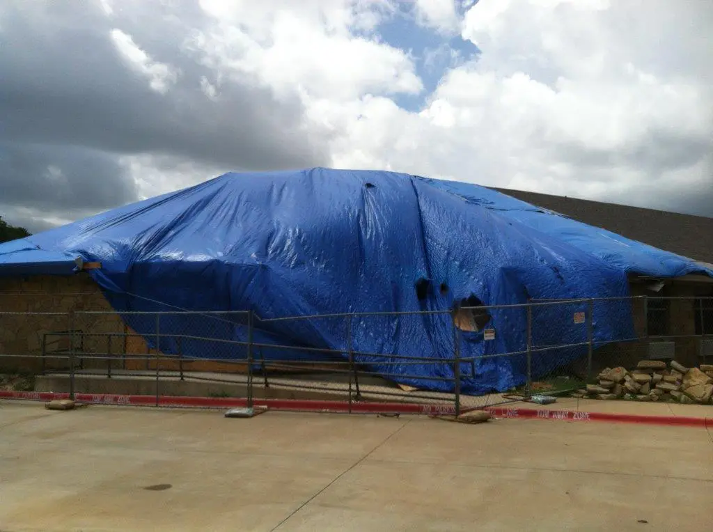 A blue tarp covering a boat in the middle of a parking lot.